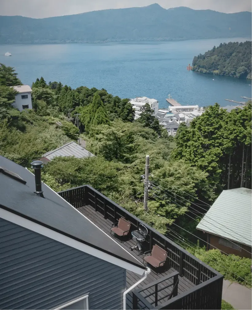 屋根とウッドデッキ越しに見下ろす芦ノ湖と箱根神社の赤い鳥居、元箱根の街並み