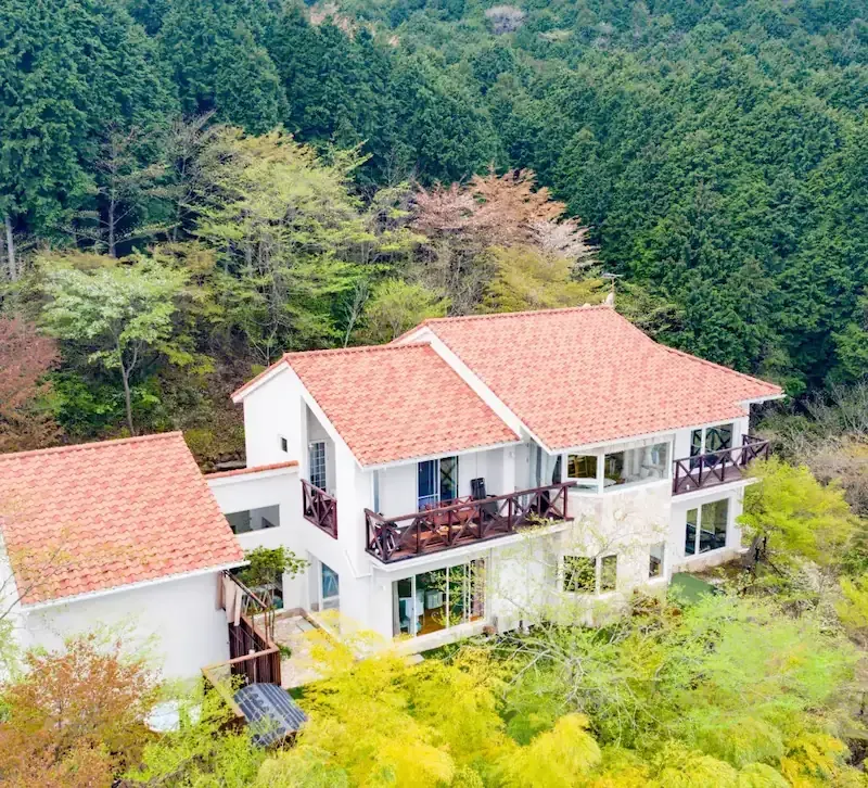 森に囲まれた敷地を上空から望む、オレンジの瓦屋根の建物全景