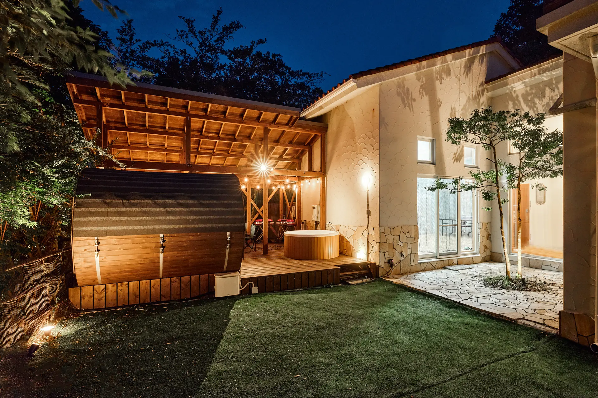 夜の外観、バレルサウナのある庭と白壁の建物