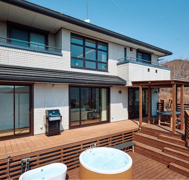 白レンガの建物前のウッドデッキに置かれたBBQグリルとジャグジー・バスタブ